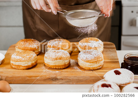 Woman chef prepares fresh donuts in her bakery. Cooking traditional Jewish Hanukkah Sufganiyot. Small business concept. 100282566