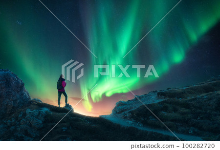 Northern lights and young woman on mountain peak at night. Auror 100282720