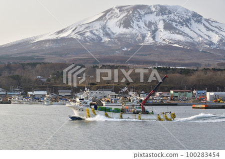 Photographing the scenery of the fishing boats leaving the Sunahara fishing port in Morimachi, Hokkaido in early spring and Mt. Sunahara in the remaining snow 100283454
