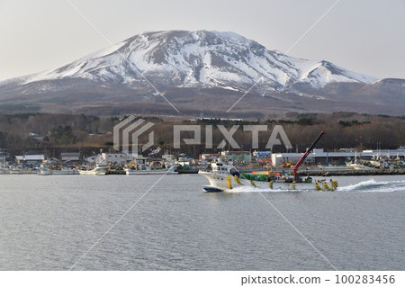 Photographing the scenery of the fishing boats leaving the Sunahara fishing port in Morimachi, Hokkaido in early spring and Mt. Sunahara in the remaining snow 100283456