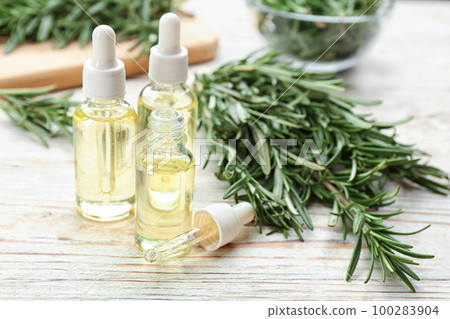 Bottles of rosemary essential oil on white wooden table 100283904