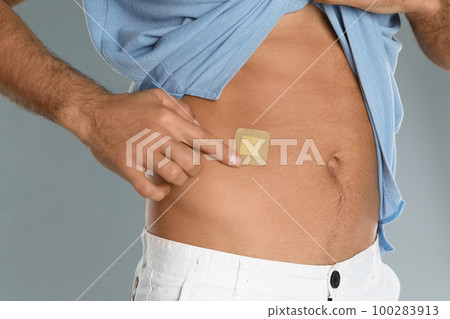 Man with sticking plaster on tummy against light grey background, closeup Man with sticking plaster on tummy against light grey background, closeup 100283913