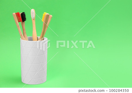 Bamboo toothbrushes in holder on green background, space for text 100284350