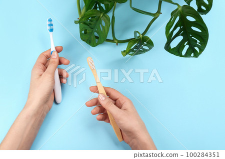 Woman holding natural bamboo and plastic toothbrushes on light blue background, above view 100284351