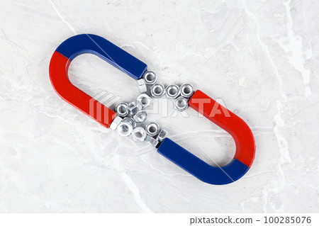 Magnets attracting metal nuts on grey marble table, flat lay 100285076