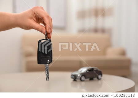 Man holding key near table with miniature automobile model indoors, closeup. Car buying 100285118