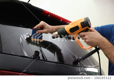 Worker tinting car window with heat gun in workshop, closeup 100285122