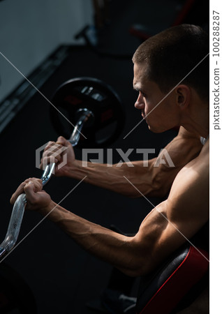 Man doing EZ barbell bicep exercises on Scott bench.  100288287