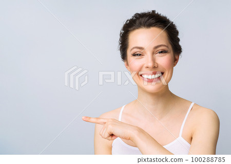 A pretty brunette with a perfect smile points to copyspace. A woman gestures on a white background. A pretty brunette with a perfect smile points to copyspace. A woman gestures on a white background. 100288785