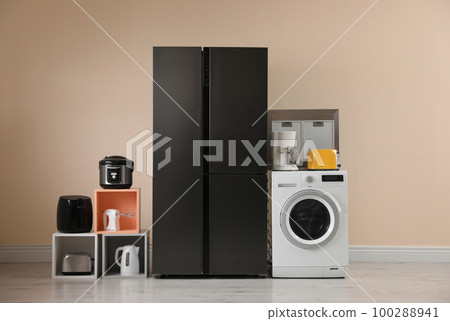 Modern refrigerator and other household appliances near beige wall indoors 100288941