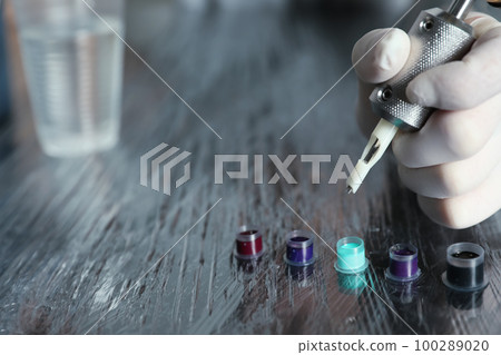Tattoo artist with machine and ink at table, closeup Tattoo artist with machine and ink at table, closeup 100289020