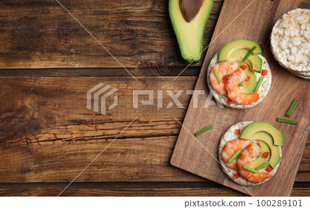Puffed rice cakes with shrimps and avocado on wooden table, flat lay. Space for text Puffed rice cakes with shrimps and avocado on wooden table, flat lay. Space for text 100289101
