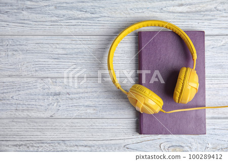 Book and modern headphones on white wooden table, top view. Space for text 100289412