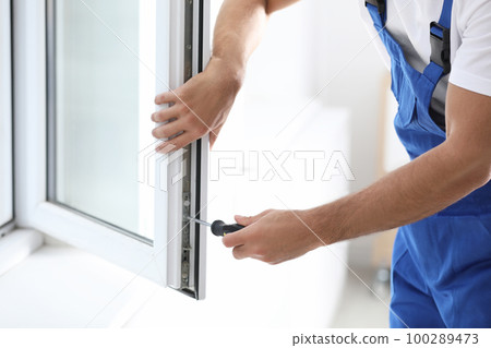 Construction worker repairing plastic window with screwdriver indoors, closeup 100289473