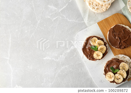 Puffed rice cakes with chocolate spread, banana and mint on grey marble table, flat lay. Space for text 100289872