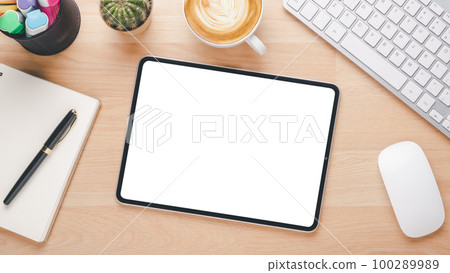 Wooden desk workplace with blank screen digital tablet, keyboard computer, mouse, pen, notebook and cup of coffee, Top view flat lay. Wooden desk workplace with blank screen digital tablet, keyboard computer, mouse, pen, notebook and cup of coffee, Top view flat lay. 100289989