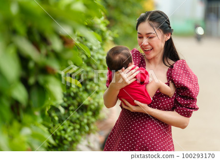 mother holding and playing with baby newborn in the garden 100293170