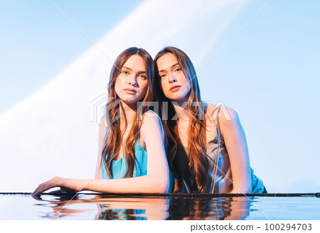 Beauty portrait with water of young girls twins sisters with dark long hair on blue background Beauty portrait with water of young girls twins sisters with dark long hair on blue background 100294703