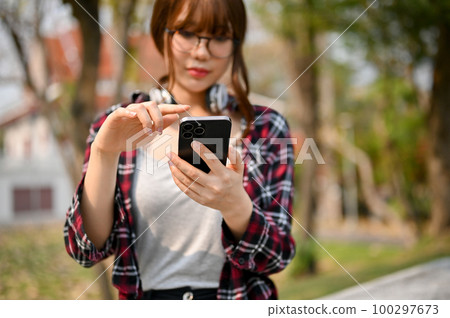 Young Asian female college student using her phone at the campus park. 100297673
