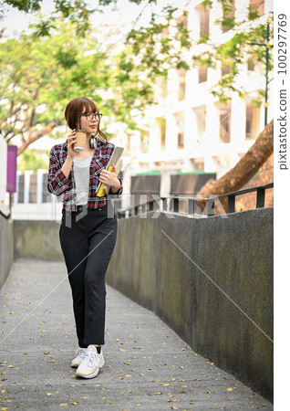Pretty Asian female college student walking along the campus building with her takeaway coffee 100297769