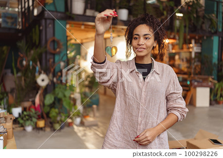 Smiling woman holding handmade glass decoration in the form of heart standing in home decor studio Smiling woman holding handmade glass decoration in the form of heart standing in home decor studio 100298226