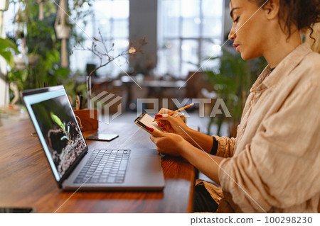 Florist woman works in her small floral business surf for information about plants using laptop 100298230