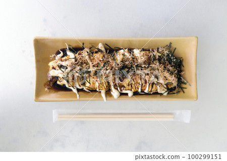 Gyuhei Yaki, stir fried vegetable wrapped with egg and meat on ceramic plate place next to bamboo chopstick on white table. Top View 100299151