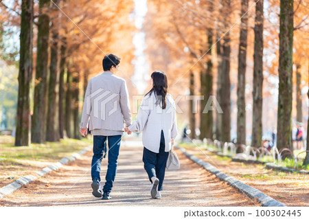 年輕夫婦手牽手走在綠樹成蔭的街道上 100302445