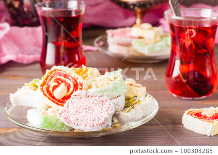 Traditional Turkish Delight. on a plate and hot karkade in cups on a wooden table Traditional Turkish Delight. on a plate and hot karkade in cups on a wooden table 100303285