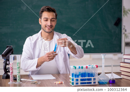 Young male chemist in front of green board 100312364