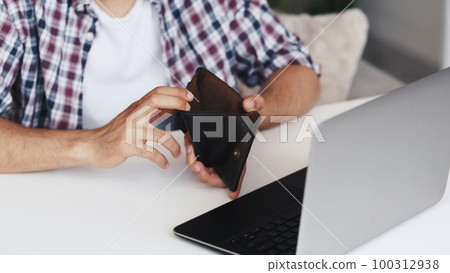 Internet scam. Online fraud. Freelance work risk. Unrecognizable broke poor man hands revealing empty wallet at workplace with laptop. Internet scam. Online fraud. Freelance work risk. Unrecognizable broke poor man hands revealing empty wallet at workplace with laptop. 100312938