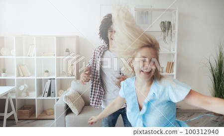 Couple fun. Crazy weekend. Happy moments. Defocused joyful excited girl dancing with boyfriend at light morning home interior with copy space. 100312940