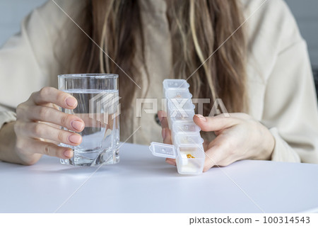 Woman is holding a Medication organizer with an open cell and is about to drink her daily dose of medication. Pill box, case, holder, container or caddy. 100314543