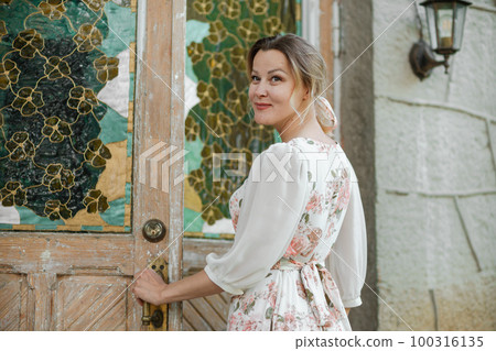 woman in a flower dress opens the door to the house woman in a flower dress opens the door to the house 100316135