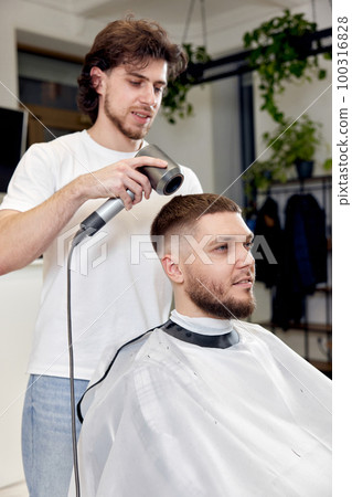 Professional hairdresser during work with man client with hair dryer 100316828