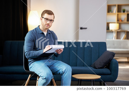 Portrait of happy male psychologist looking at camera and taking notes during therapy session at clinic. Friendly psychotherapist posing and smiling at office 100317769