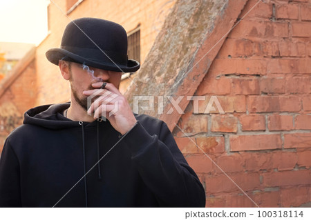Young man in a hat smoking a cigarette on a city street. Young man in a hat smoking a cigarette on a city street. 100318114