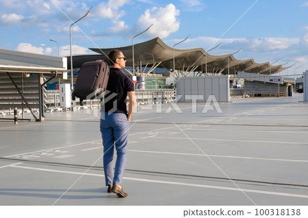 A young man with a suitcase walks in the parking lot outdoors. Business trip, vacation A young man with a suitcase walks in the parking lot outdoors. Business trip, vacation 100318138