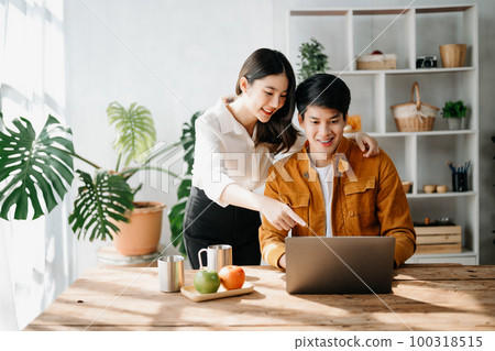 Two Asian business workers talking on the smartphone and using laptop at the home office. 100318515