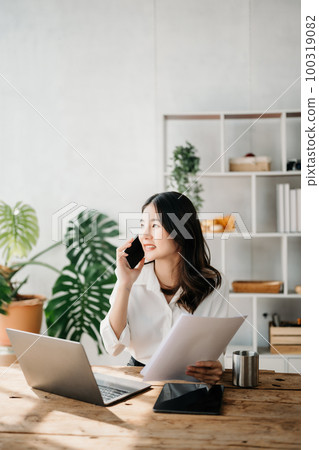 Business asian woman Talking on the phone and using a laptop with a smile while sitting at home office Business asian woman Talking on the phone and using a laptop with a smile while sitting at home office 100319082