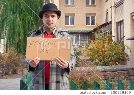 Middle-aged man with a sign in his hands Forgive me on a city street. Forgiveness concept 100319369