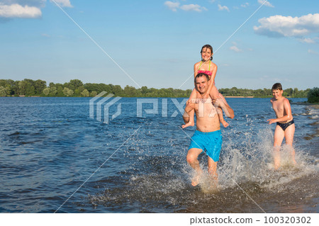 Happy family having fun on the beach running and jumping in the water at sunset. Summer vacation, lifestyle 100320302