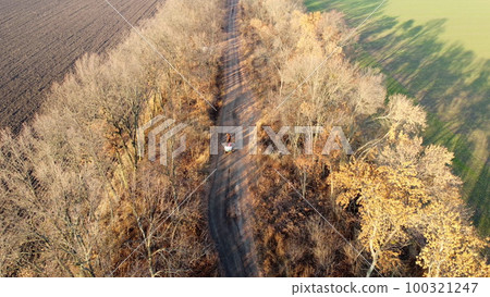 People riding in cart carriage with sacks and horses driving along dirt country road between trees without leaves on autumn sunny day. Rural countryside landscape, country scenery. Aerial drone view People riding in cart carriage with sacks and horses driving along dirt country road between trees without leaves on autumn sunny day. Rural countryside landscape, country scenery. Aerial drone view 100321247