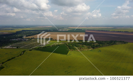 Green and yellow agricultural farm fields, fast moving shadows on the earth from white clouds in sky on a summer day. Agricultural panoramic landscape. Agrarian plantations scene. Aerial drone view. 100321377