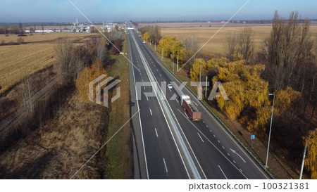 Cars driving along the highway on an autumn sunny day. Automobile road with white markings between agricultural fields. View of the cars driving on paved road. automobile vehicles. Aerial drone view. Cars driving along the highway on an autumn sunny day. Automobile road with white markings between agricultural fields. View of the cars driving on paved road. automobile vehicles. Aerial drone view. 100321381