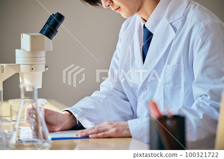 A young man in a white coat taking notes on experimental data A young man in a white coat taking notes on experimental data 100321722