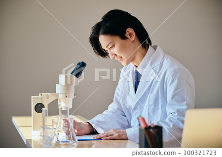 A young man in a white coat taking notes on experimental data 100321723
