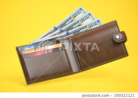 Open leather wallet with dollars and credit cards on yellow background. 100322121
