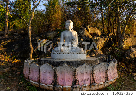 White meditating Buddha statue sits on the rock pile among forest trees in the afternoon time at India. Great religious architecture. White meditating Buddha statue sits on the rock pile among forest trees in the afternoon time at India. Great religious architecture. 100324359