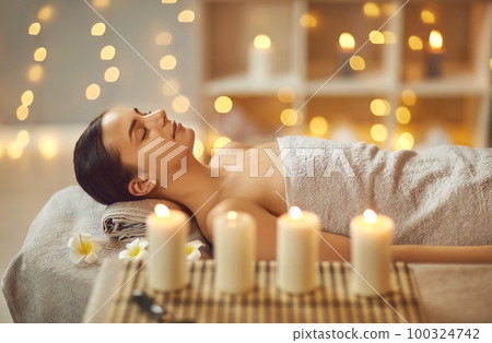 Young woman lying with closed eyes alone on massage couch in salon at wellness center. Young woman lying with closed eyes alone on massage couch in salon at wellness center. 100324742